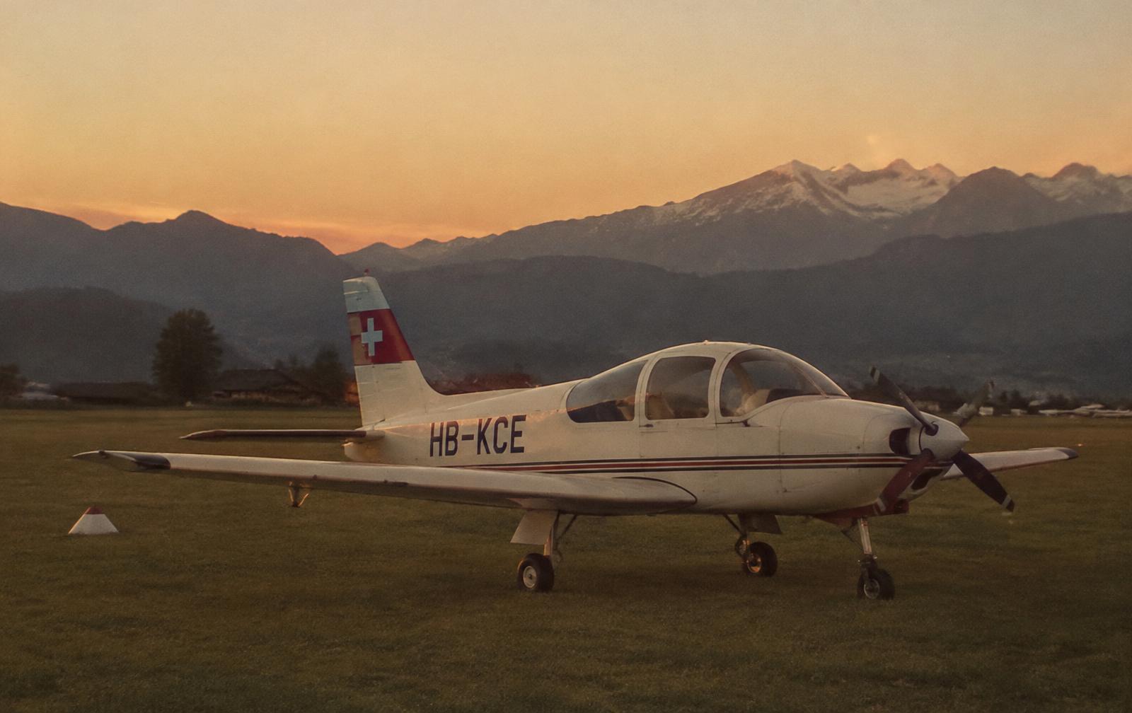 Small Swiss training aircraft on a grass airfield at dusk